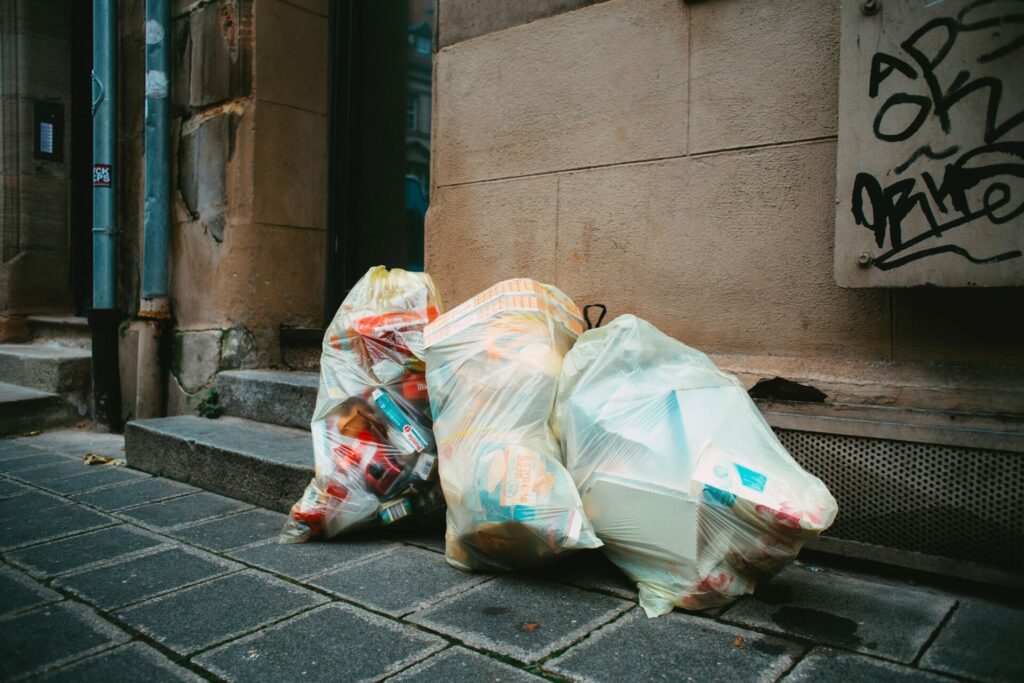 three full trash bags on the street leaning up against a building.