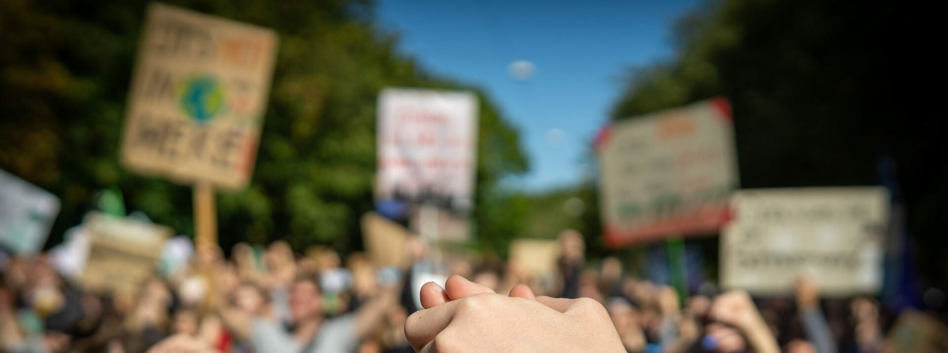 Two people at a rally, joining hands together signaling peace, unity and decisiveness in front of a crowd carrying protest placards with shallow depth of field