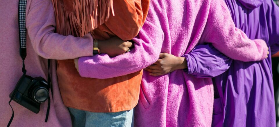 Four friends, not facing the camera. Arms around each others backs in solidarity