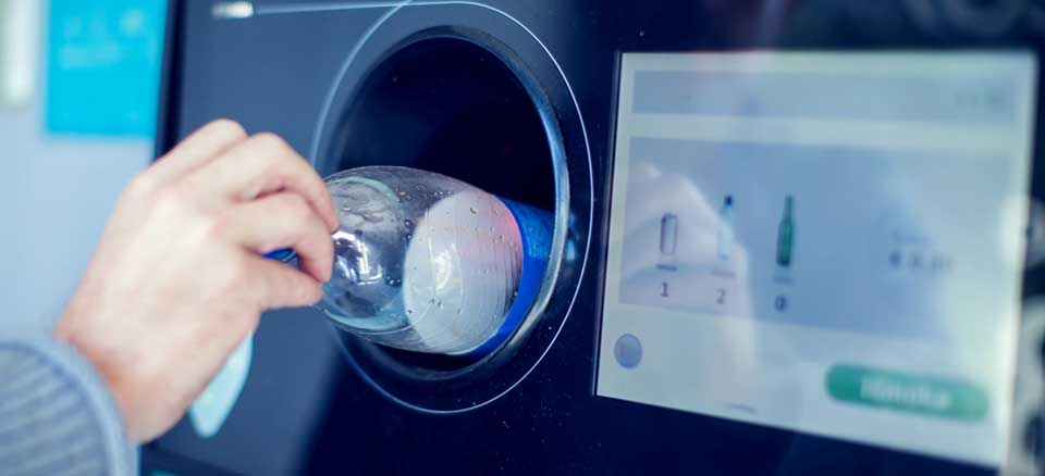 Person returning empty bottle at reverse vending machine as part of the Bottle Bill program