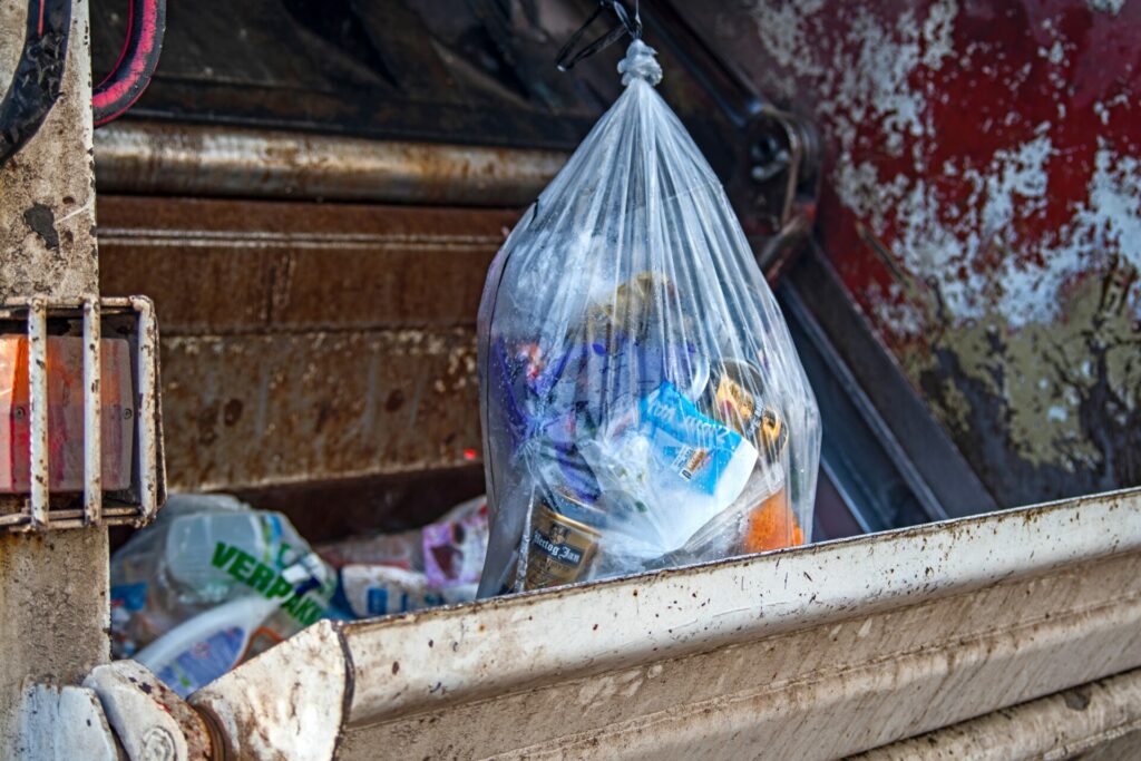 Bag of trash being dumped in a garbage truck. 