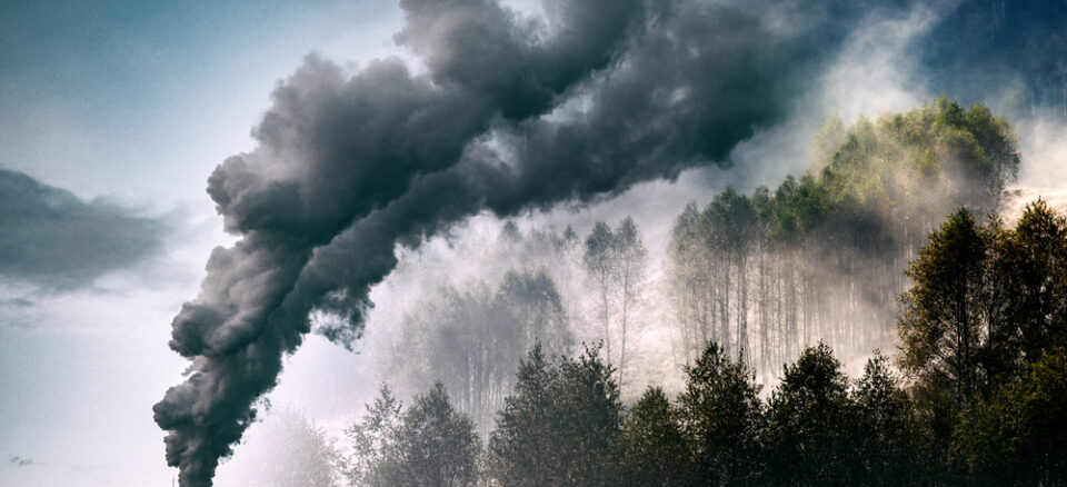 Climate-damaging emissions coming from smokestack and covering green forest