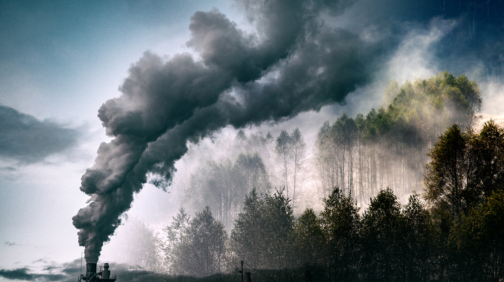 Climate-damaging emissions coming from smokestack and covering green forest