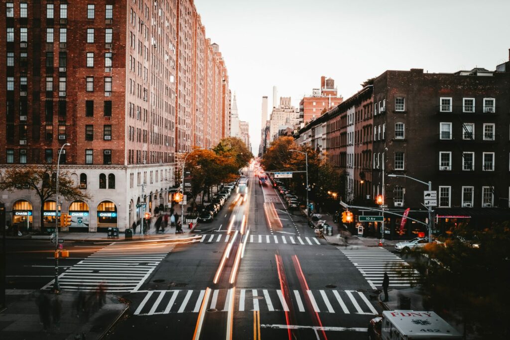 Brick buildings on the right and left with the center a road with crosswalks and moving cars