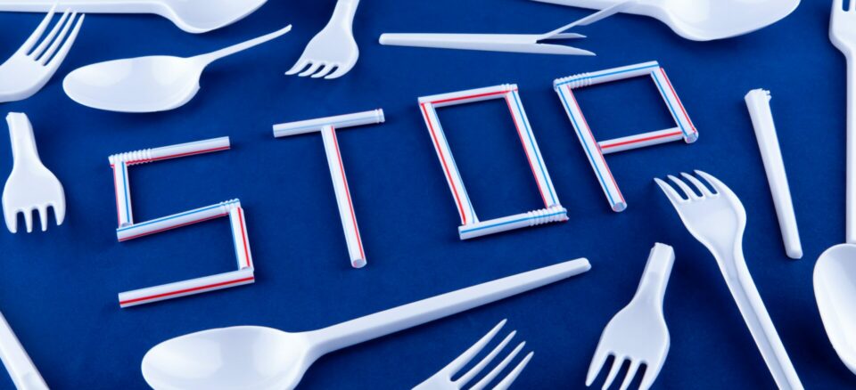 The word stop made of plastic tubes on a blue background with plastic utensils environmental pollution concept. Top view