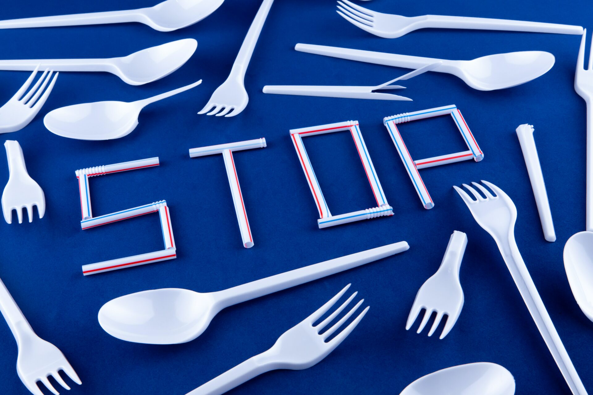 The word stop made of plastic tubes on a blue background with plastic utensils environmental pollution concept. Top view