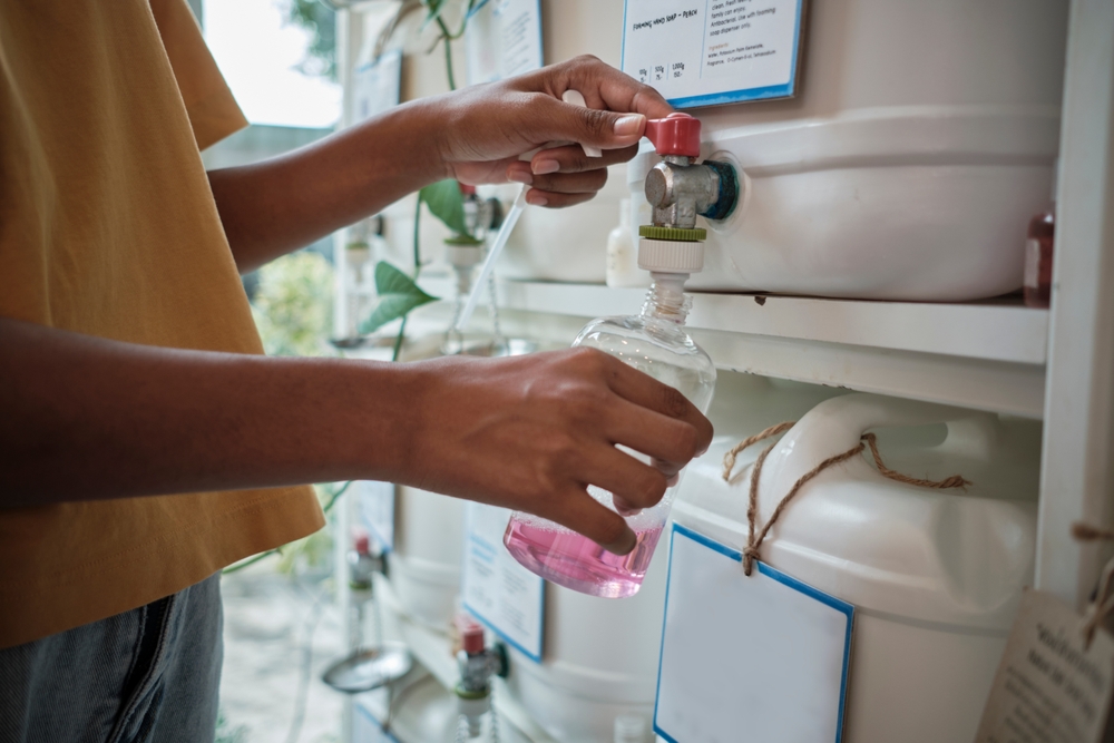 Close-up shot of customers' hands filling natural products into a recycling bottle from reusable containers in zero-waste and refill store, environment-friendly retail shop, and sustainable lifestyle.