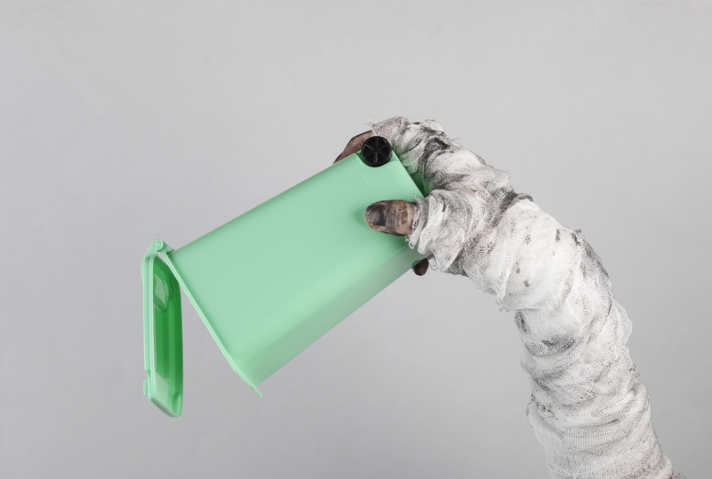 Monster's hand wrapped in a bandage holding trash can isolated on gray background.