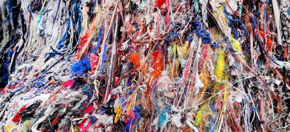 Mountain of colorful textile waste that includes strings, fabrics, and miscellaneous fibers.