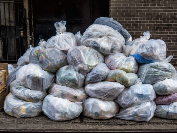 Pile of translucent trash bags on a sidewalk.