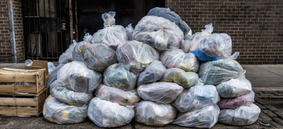 Pile of translucent trash bags on a sidewalk.