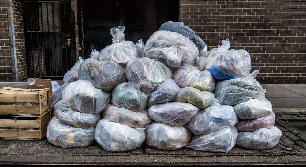 Pile of translucent trash bags on a sidewalk.