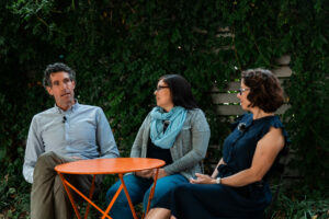 Three Just Zero staff members outside talking at a small round, orange table
