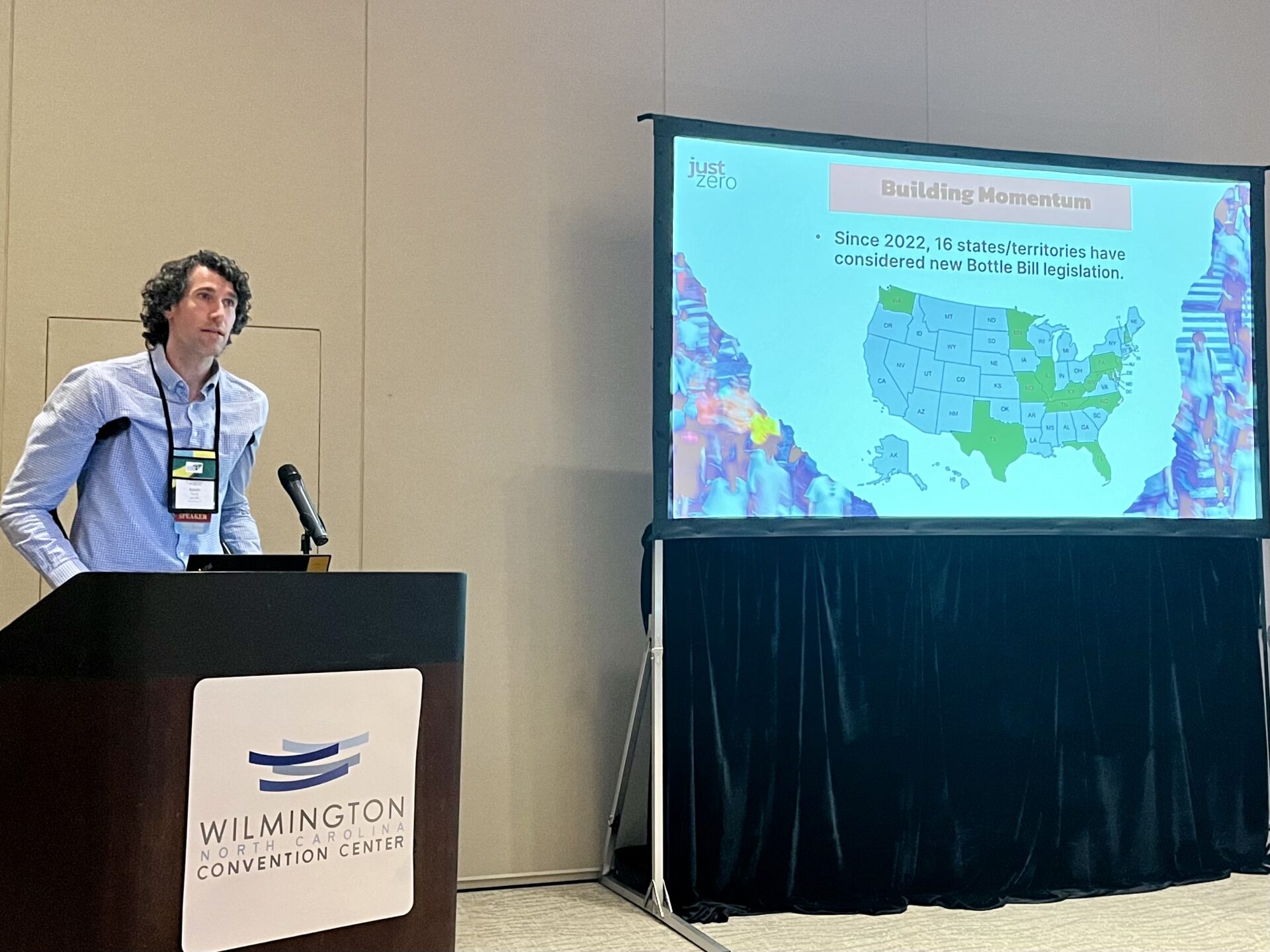 Man with dark, curly hair presenting at a convention.
