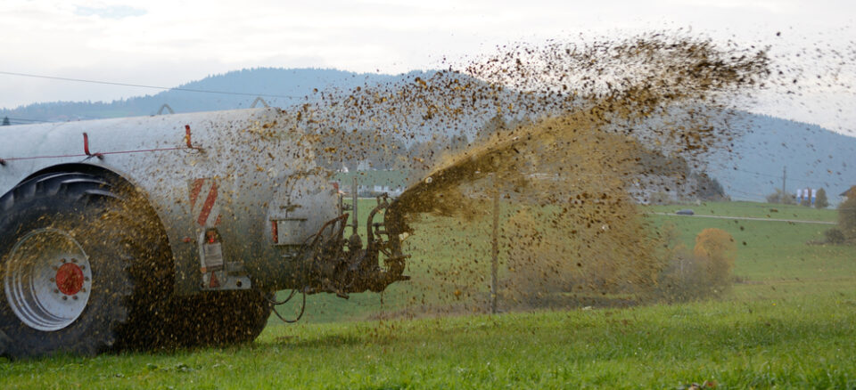 Tractor spreading slurry across a green meadow