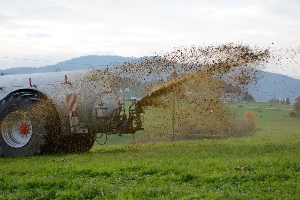 Tractor spreading slurry across a green meadow